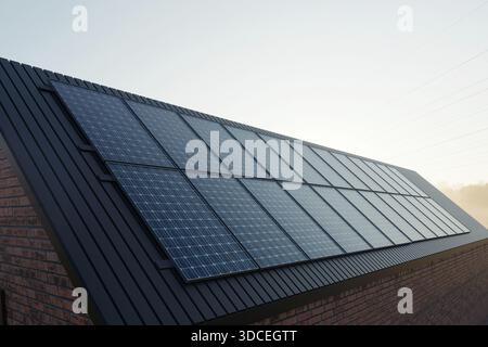 Pannelli solari installati su un elegante tetto scuro di una moderna casa in mattoni. Energia verde, efficienza domestica, impianto fotovoltaico, sostenibilità ed eco-frie Foto Stock