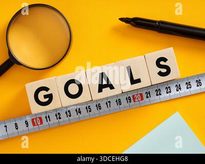 Obiettivi ortografici a cubetti di legno con metro a nastro, che rappresentano la definizione e il raggiungimento degli obiettivi Foto Stock