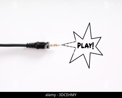 Cavo audio nero con punta dorata che punta a un comico Riproduci! simbolo, che rappresenta l'attivazione del suono e il coinvolgimento dei contenuti multimediali Foto Stock