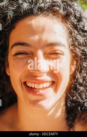 Primo piano di una donna che sorride brillantemente in una calda luce naturale del sole Foto Stock