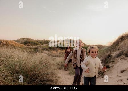 Donna e due bambini camminano attraverso dune costiere erbose Foto Stock