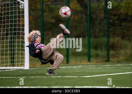 Ragazzo che calcia la palla a mezz'aria su un campo da calcio verde. Foto Stock
