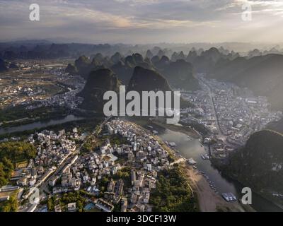 Vista aerea delle splendide montagne carsiche che si innalzano sopra il tortuoso fiume e gli edifici raggruppati, Yangshuo, Guangxi, Cina. Foto Stock