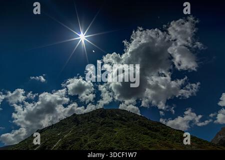 Vista del sole che splende attraverso le nuvole sopra l'aspra vetta della montagna, creando un contrasto incredibile con il cielo blu profondo, Noori Top, Khyb Foto Stock