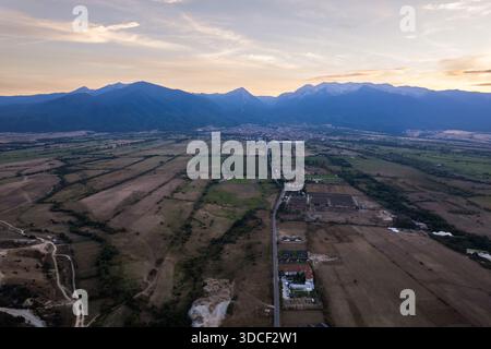 Vista aerea di vasti campi che si estendono verso l'orizzonte, incontrando le lontane montagne innevate sotto un cielo morbido e pastello, Banya, Razlog, Bulgaria. Foto Stock