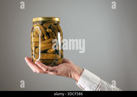 Tenendo a mano il vaso in vetro di cetriolini sottaceto, cetrioli, messa a fuoco selettiva Foto Stock