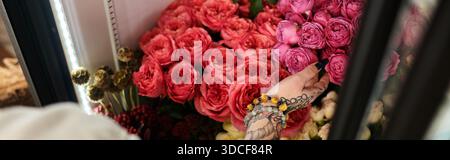 Una fiorista con tatuaggi prepara rose colorate nel suo accogliente negozio, il banner Foto Stock