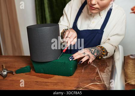 Una giovane fiorista crea una schiuma floreale in mezzo a diversi strumenti nel suo negozio Foto Stock
