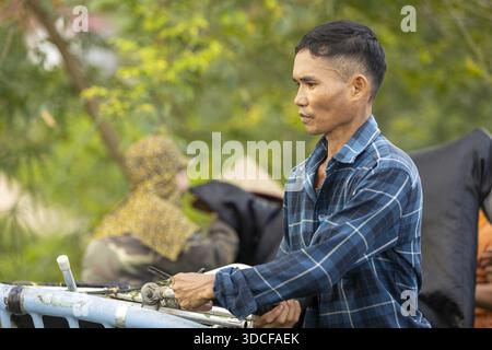 Phu Tho, Vietnam - 15 ottobre 2025: La vista di un uomo con una camicia blu a quadri, con attrezzatura messa a fuoco e in mano, si distingue contro il morbido e sfocato backgroun Foto Stock