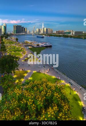 Vista aerea del fiume Saigon che risplende, riflettendo lo skyline della città, con il punto di riferimento 81 che perfora il cielo e una vivace passeggiata pullulante di vita, Foto Stock