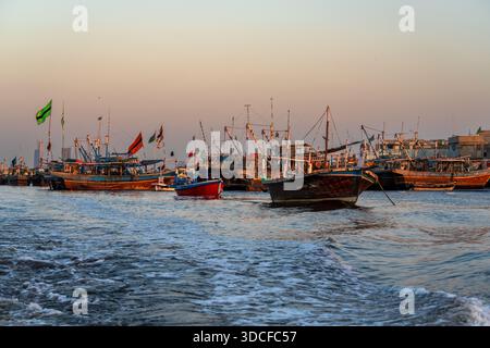 Karachi, Pakistan - 21 novembre 2024: Vista delle barche da pesca che rimbalzano dolcemente sull'acqua, le loro bandiere colorate sventolano nella brezza contro la sof Foto Stock