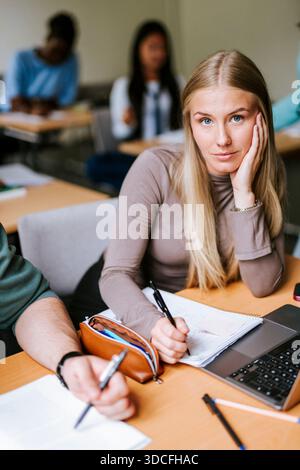 Ritratto di donna bionda appoggiata al gomito seduta in classe universitaria Foto Stock