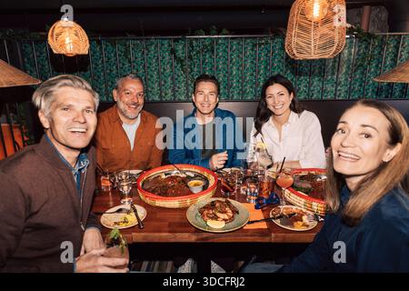 Gruppo di amici felici che si godono cibo e bevande seduti al tavolo del ristorante Foto Stock