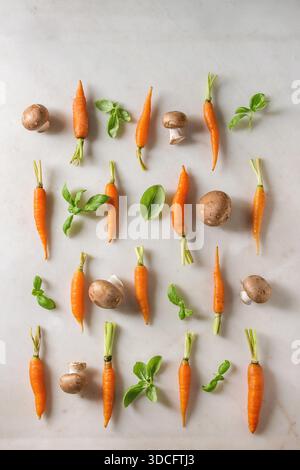Erbe fresche di basilico con piccole carote e funghi champignon in file su sfondo di marmo bianco. Piatto, spazio. Concetto di cucina, background gastronomico. Foto Stock