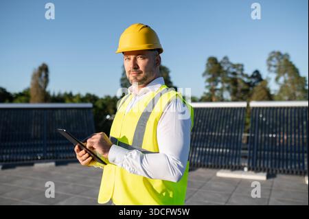 Operatore che ispeziona i pannelli solari sul tetto tenendo in mano il tablet digitale Foto Stock