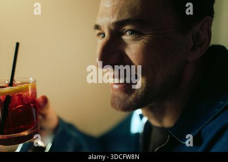 Primo piano di un uomo felice che guarda lontano mentre tiene un bicchiere da drink al ristorante Foto Stock