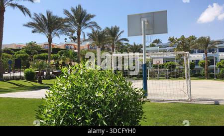 Un gol da calcio si trova su un campo erboso vicino a un campo da pallacanestro. Le palme circondano l'area e gli edifici sono visibili sullo sfondo sotto un clea Foto Stock