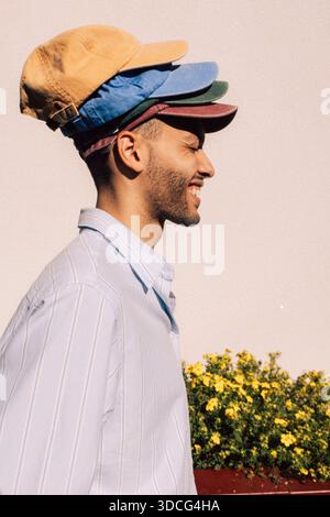 Vista laterale di un giovane giocoso che indossa cappellini multicolore contro la parete Foto Stock
