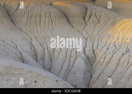 Vista delle formazioni di terra pallide e strutturate, scolpite dal tempo e dal tempo, sotto il caldo bagliore del sole che tramonta a Senek, regione di Mangystau, Kazakistan Foto Stock