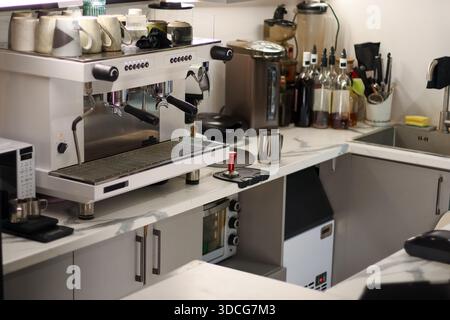 Il bancone in marmo del caffè è dotato di macchina espresso, tazze, bottiglie, caraffa e vari elettrodomestici da cucina in un ambiente moderno e ben illuminato Foto Stock