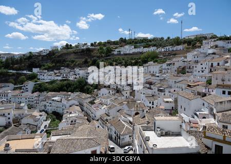 Una vista panoramica di un villaggio imbiancato con tetti in terracotta, annidato in un paesaggio collinare sotto un cielo blu luminoso con soffici nuvole Foto Stock