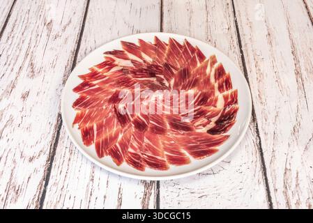 Fette di prosciutto iberico nutrito con ghiande su una tavola di legno, giocando con texture e toni tra la carne magra e il grasso marmorizzato. Foto Stock