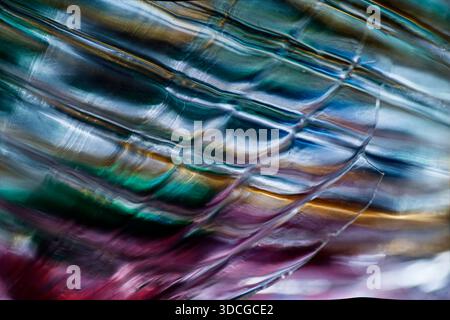 Primo piano astratto di vetro traslucido ondulato con motivi ondulati che riflettono sfumature iridescenti di blu, verde, oro, viola e rosso, creando l Foto Stock