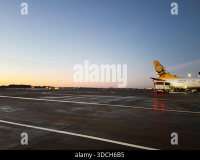 Manchester, Regno Unito - 13 dicembre 2025: Il tramonto all'aeroporto di Manchester mostra un velivolo con logo giallo delle api con equipaggio di terra e luci Foto Stock