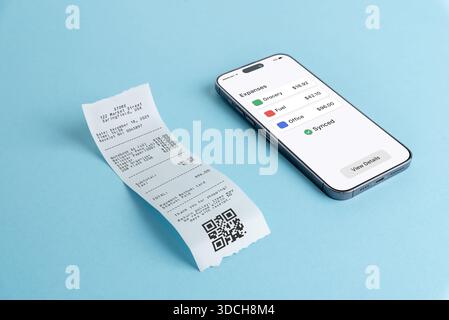 Smartphone che mostra il dashboard della panoramica delle spese accanto alla ricevuta cartacea su sfondo blu, che illustra l'app di finanza mobile, il software di contabilità e di Foto Stock