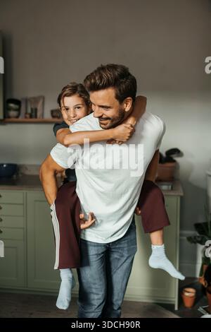 Ritratto di una ragazza sorridente che riceve un giro in piggyback dal padre a casa Foto Stock