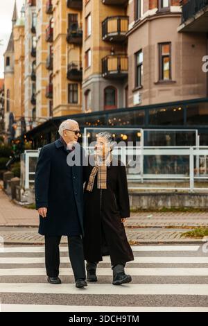 Una coppia di anziani sorridente che cammina su un incrocio a piedi in strada Foto Stock