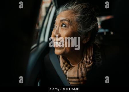 Donna anziana felice che viaggia in auto mentre guarda fuori dal finestrino Foto Stock
