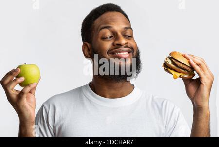 Guy Holding Burger and Apple Choosing Food, sfondo bianco Foto Stock
