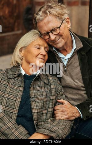 Donna anziana sorridente che passa il tempo libero appoggiandosi all'uomo con gli occhi chiusi Foto Stock