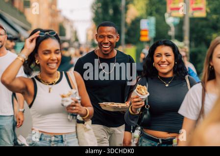 Uomo felice che tiene il cibo da asporto camminando con gli amici alla festa di strada Foto Stock