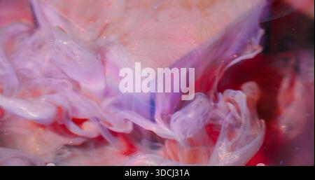 Goccia di inchiostro brillante. Miscela di fluido sfocato. Versamento di liquido colorato sul cubo artistico. Pigmento rosa viola rosso sott'acqua che scioglie lo sfondo astratto. Foto Stock