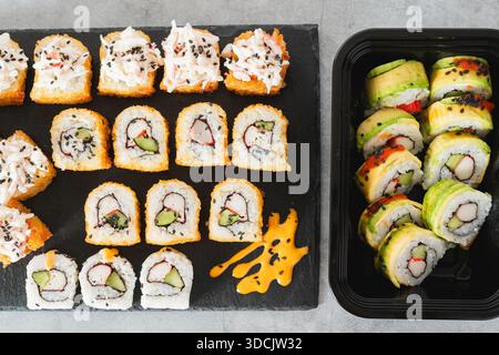 Assortimento di sushi Rolls, incluse le versioni fritte e con rivestimento in avocado, disposti su un vassoio in ardesia nera e plastica Foto Stock