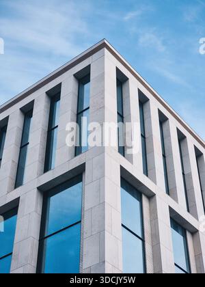 Affacciandosi sulla facciata di un edificio moderno con facciata in piastrelle di pietra. Angolo di elegante edificio residenziale con alte finestre; giorno di sole, cielo blu. Foto Stock