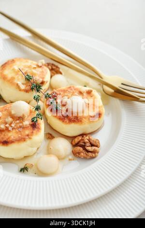 Piatto bianco con frittelle di formaggio fresco, sciroppi, frittelle di cagliata servite con palle di pera, noci e miele su sfondo chiaro, vista dall'alto Foto Stock