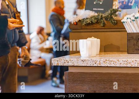 Tazze in ceramica bianca siedono su un banco in pietra all'interno di una caffetteria affollata decorata con ghirlande e tinsel natalizi Foto Stock