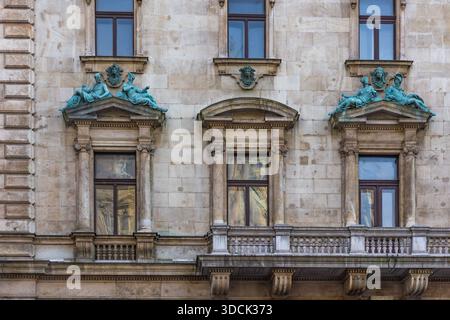 Immagine orizzontale da vicino di una facciata in pietra con finestre classiche, balconi decorativi e sculture allegoriche in bronzo verde Foto Stock