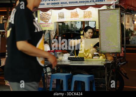 Khao Lak, Tailandia, 24 11 2025: Foto di strada per piccole imprese - la donna tailandese prepara tradizionali focaccine tailandesi asiatiche, Roti pancake chiosco con carrello stradale Foto Stock