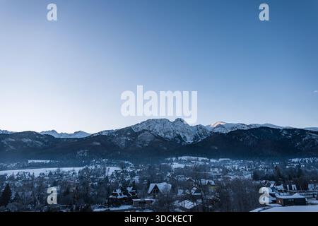 Vista panoramica della nebbiosa cittadina innevata di Zakopane, annidata sotto le torreggianti cime rocciose dei Monti Tatra, in Polonia. Blu chiaro Foto Stock