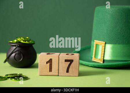 Concetto di giorno St Patricks con cappello verde Leprechaun, monete in pentola nera, festeggiano la data al blocco di legno su sfondo verde. Primo piano. Copia spazio. Foto Stock