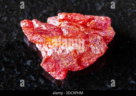 Assaggio di minerale grezzo realgar su fondo di granito nero da vicino da Altai, Russia Foto Stock