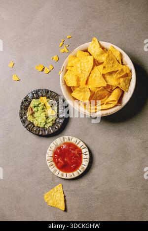Tortilla nachos corn chips con avocado guacamole e salsa di pomodoro servita nel recipiente di ceramica piastra sulla texture marrone dello sfondo. Laici piana, spazio Foto Stock