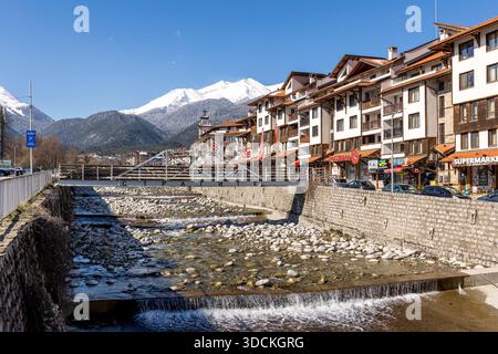 Bansko, Bulgaria - 9 aprile 2025: Fiume Glazne nella città bulgara, case alberghiere e cime innevate dei monti Pirin Foto Stock