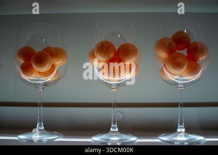 Tre bicchieri da vino pieni di albicocche arancioni disposti in fila su una superficie interna minimale, composizione pulita e luce naturale soffusa. Foto Stock