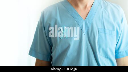 Primo piano di medico maschile che indossa l'uniforme medica con nastro di raso blu. Striscione isolato su bianco. Novembre il concetto del mese di sensibilizzazione sul cancro alla prostata, la prevenzione, la diagnosi precoce e il trattamento oncologico Foto Stock