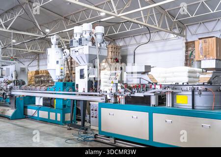 Macchina per la produzione di estrusione plastica in una moderna fabbrica industriale, linea di lavorazione automatizzata dei polimeri per la produzione di prodotti in plastica con materie prime e pannelli di controllo. Foto Stock